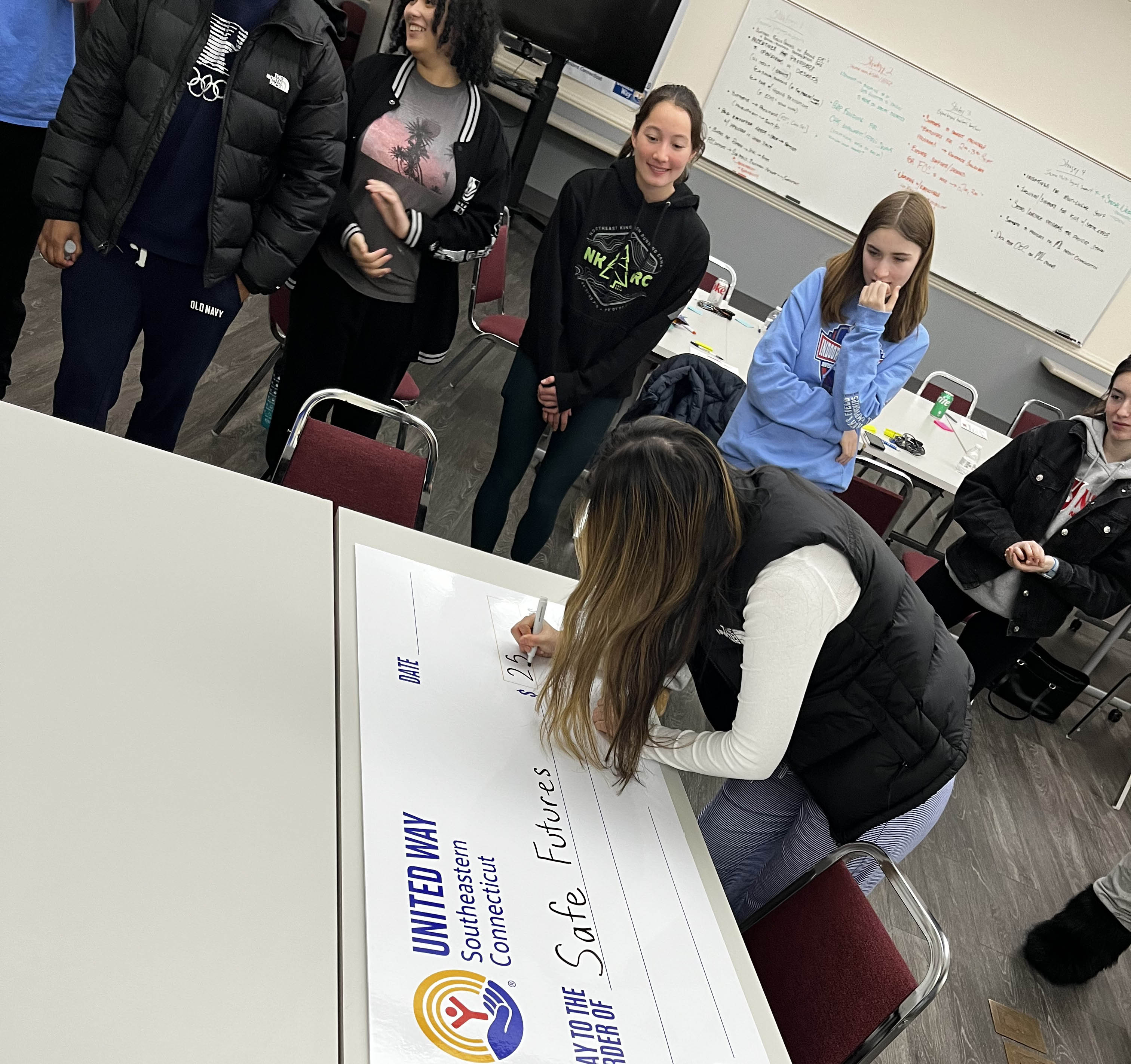 Student United Way participants gather around a table as one of the fills out the presentation check to Safe Futures
