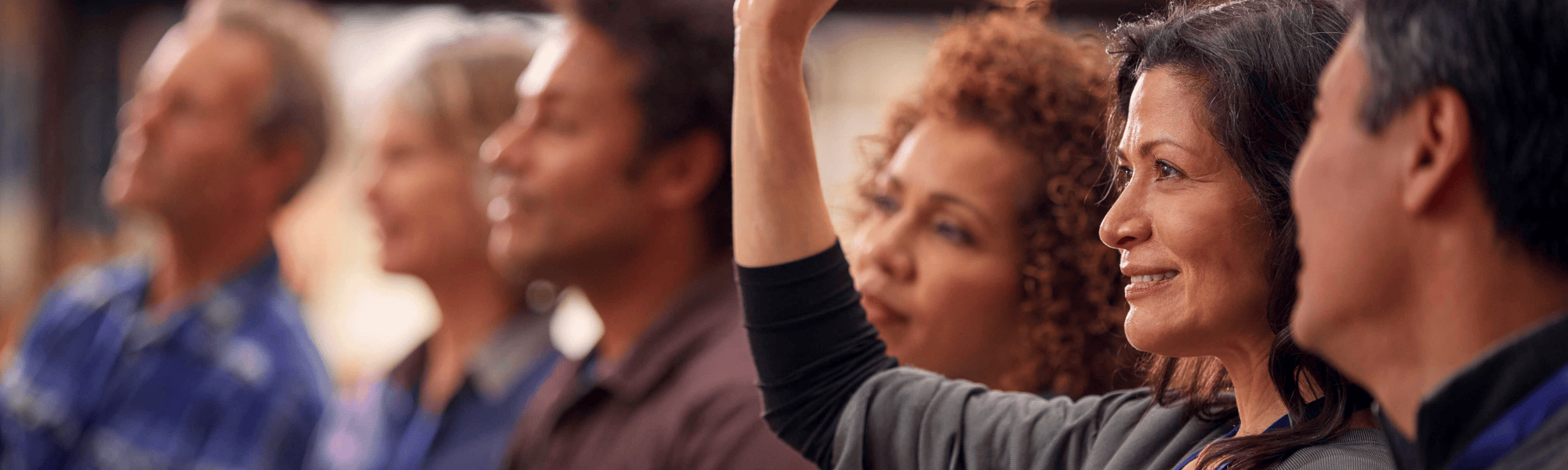 Several individuals listening to a speaker with one person's hand raised