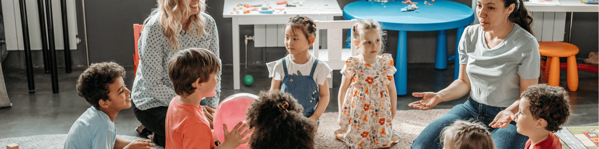 Two childcare workers interacting with young children sitting on the floor in a circle