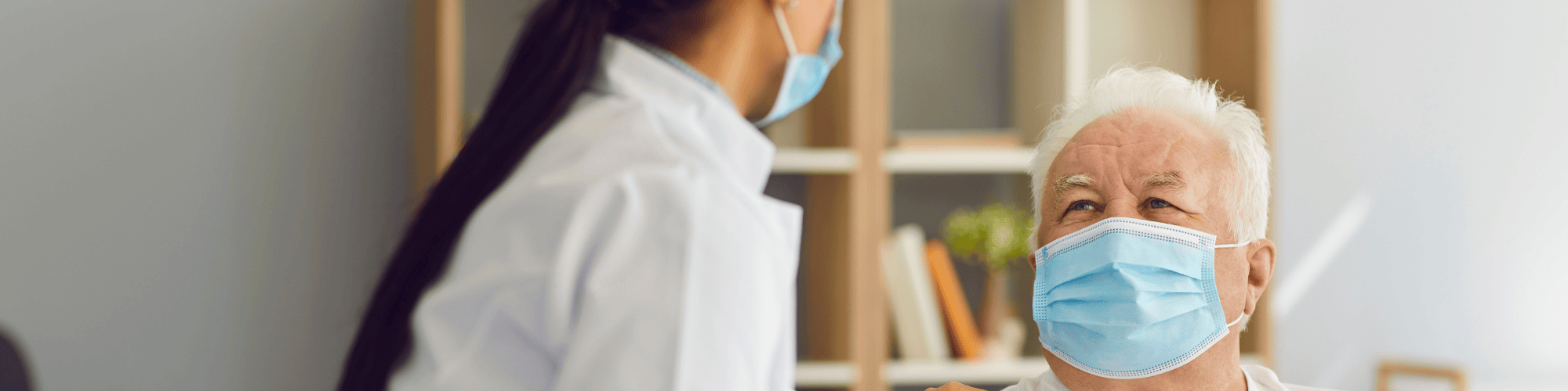 A doctor speaking with an elderly man with her hand on his shoulder