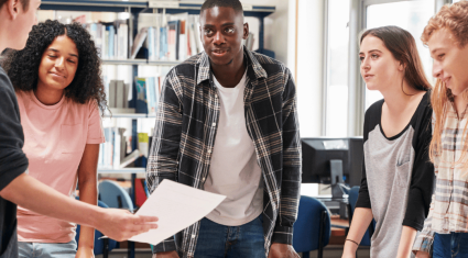 Students standing and having a conversation around a table with papers on the table